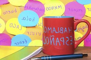 A coffee mug on a desk that says "Hablamos espanol".