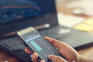 A person comparing financial stocks on a smart phone and a laptop.