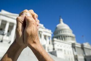 Two hands clasped together in front of a state capital building.