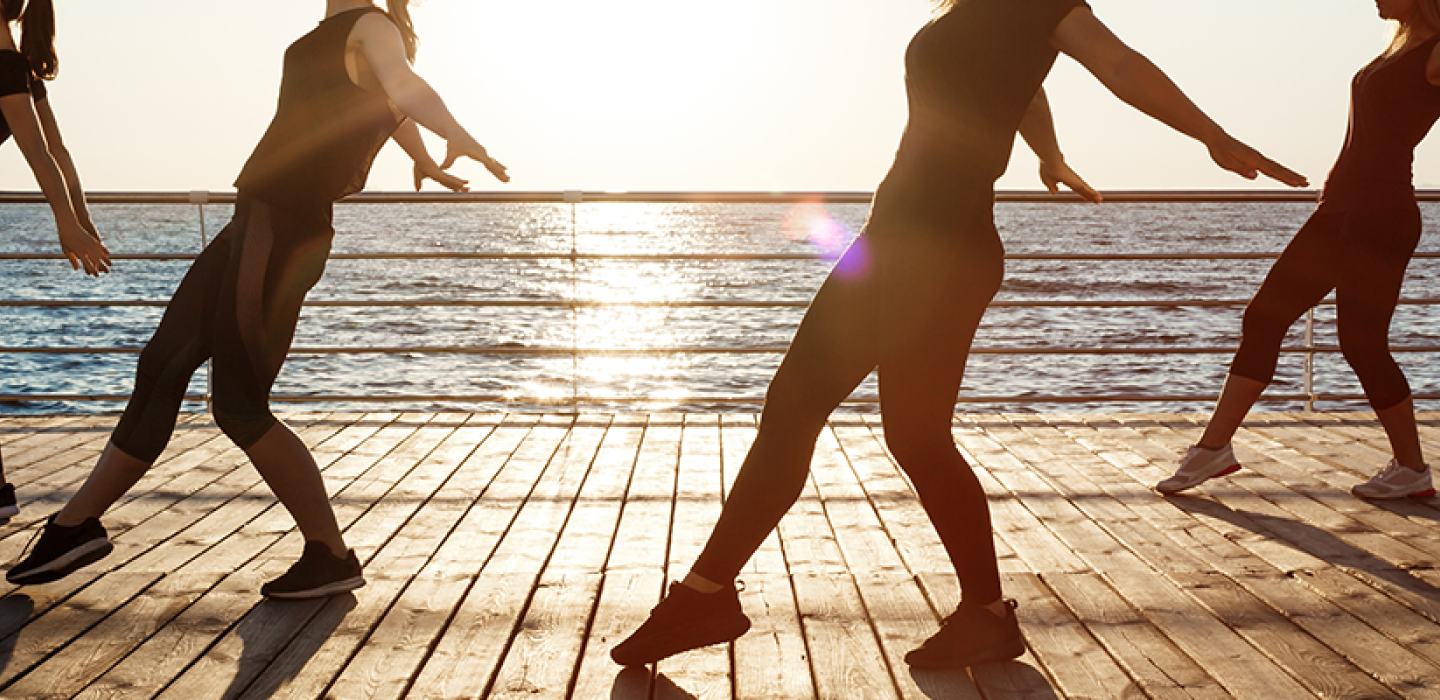 Silhouettes of sportive women dancing near sea at sunrise